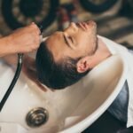 Cropped view hairstylist washing clients hair in barber shop