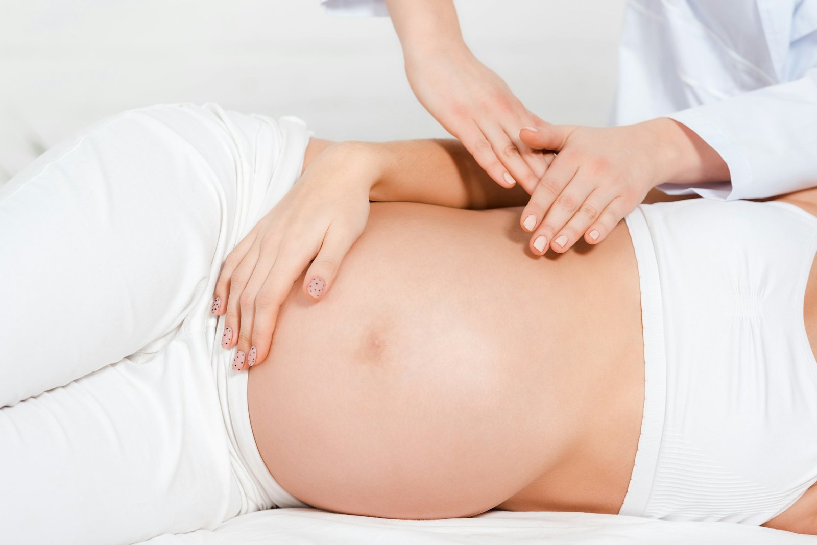 Cropped view of masseur doing massage of belly to pregnant girl on massage table