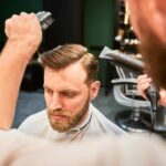 Experienced barber using hairdryer with brush to style hair.