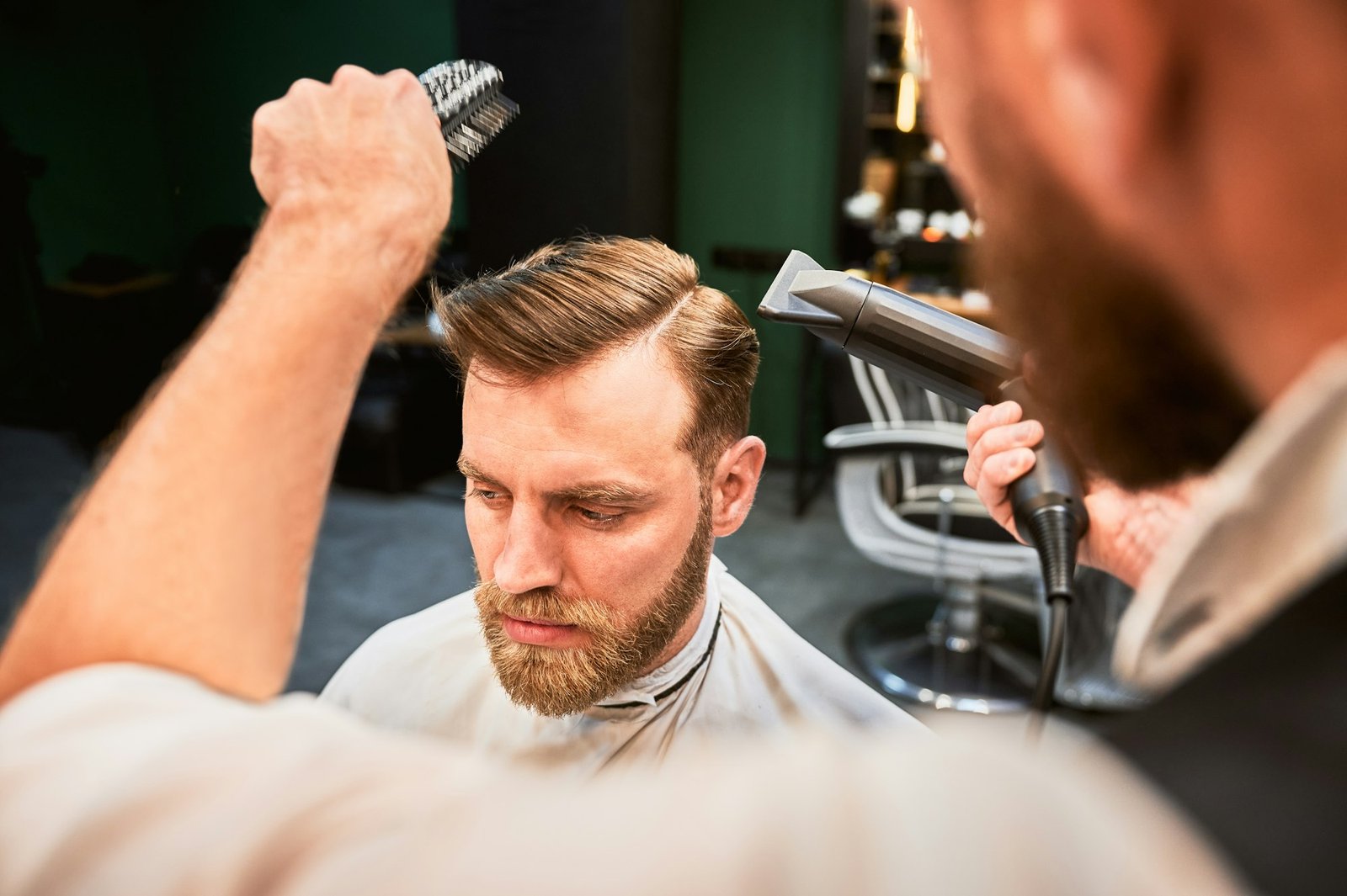 Experienced barber using hairdryer with brush to style hair.