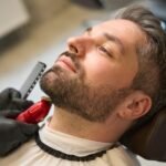 Man with stylish haircut waiting barber trimming neckline, modeling his beard