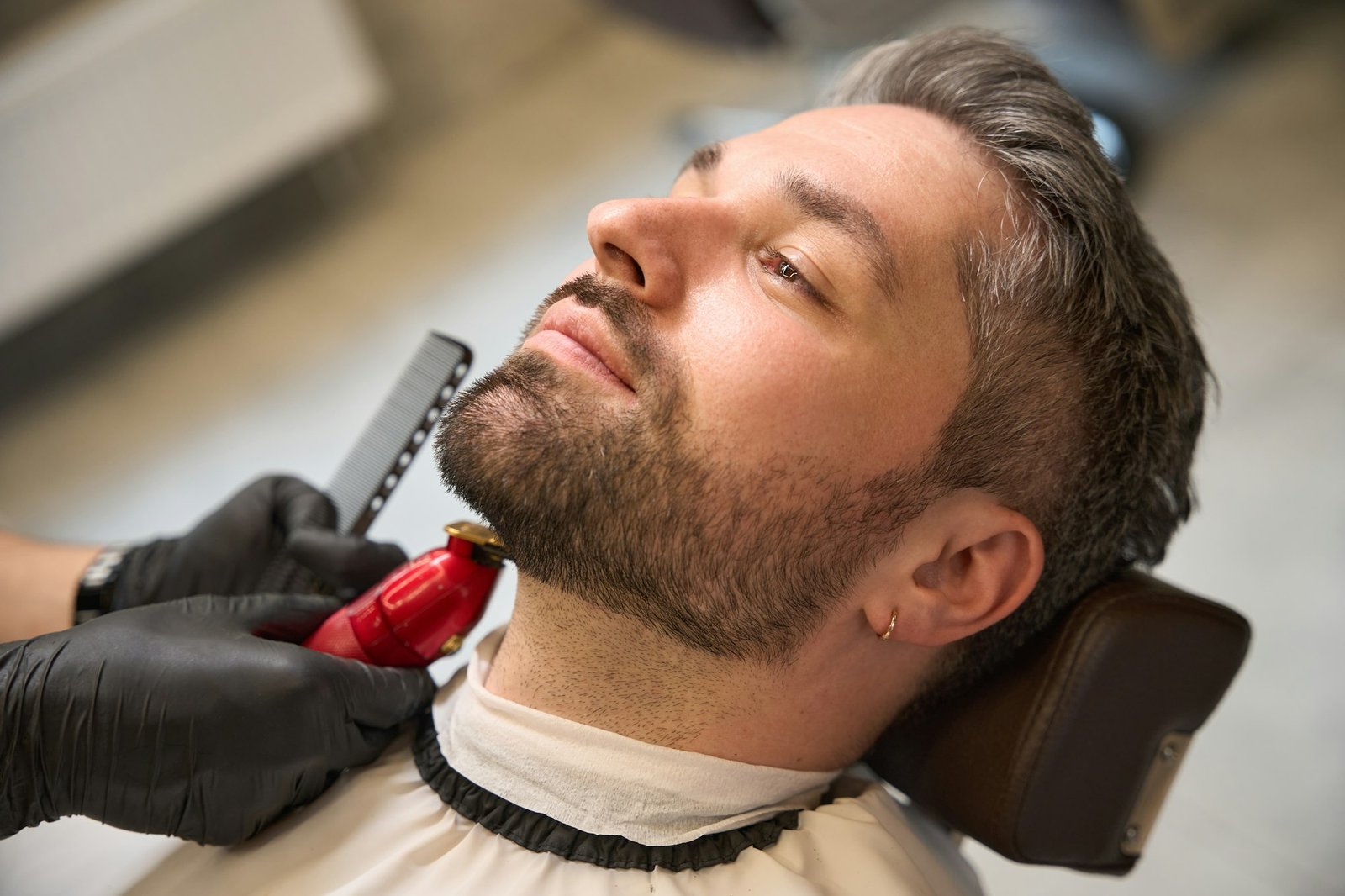 Man with stylish haircut waiting barber trimming neckline, modeling his beard