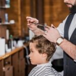 side view of barber cutting hair of curly little kid