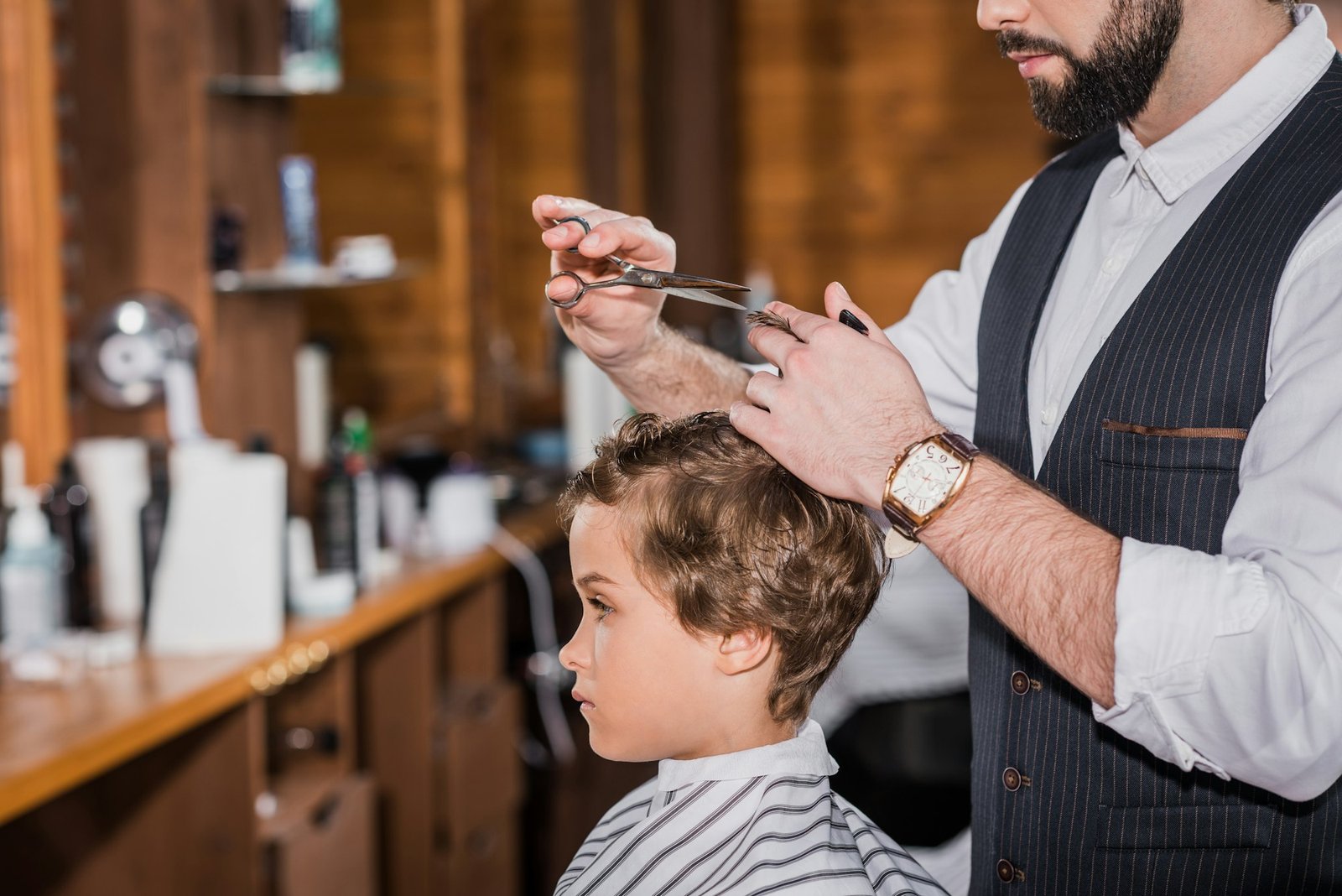 side view of barber cutting hair of curly little kid