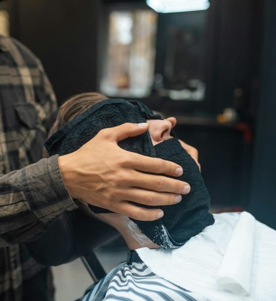 Barber preparing man face for shaving with hot towel in barber shop