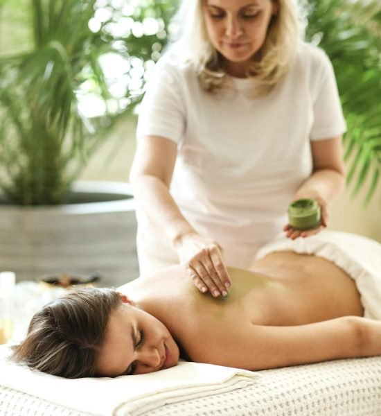 Beautiful relaxed woman having clay mask applying to the back