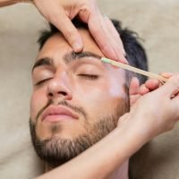 Crop beautician waxing eyebrows of male client