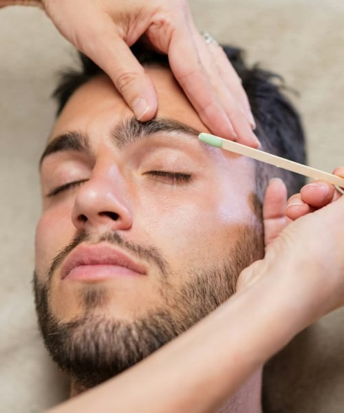 Crop beautician waxing eyebrows of male client