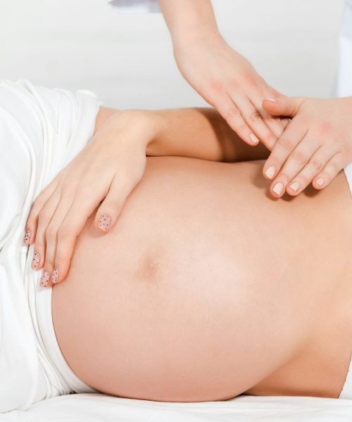 Cropped view of masseur doing massage of belly to pregnant girl on massage table