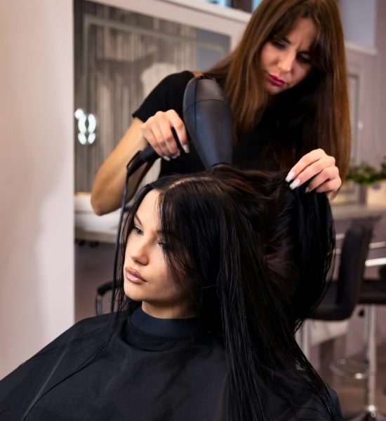 Hairstylist using black hair dryer in spa salon for hairstyle lovely brunette lady