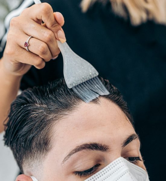 Hand of a hairdresser using a brush to coloring the hair of a man on a salon