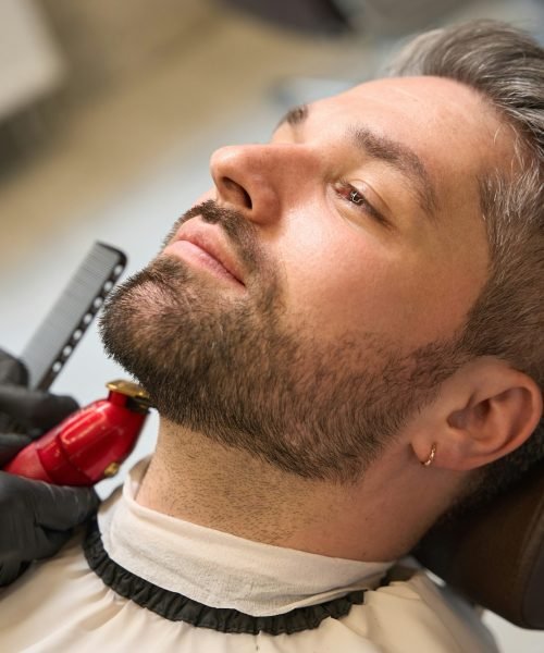 Man with stylish haircut waiting barber trimming neckline, modeling his beard