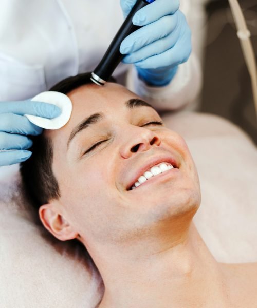 Profession cosmetologist making vacuum facial skin cleaning for smiling man in beauty salon