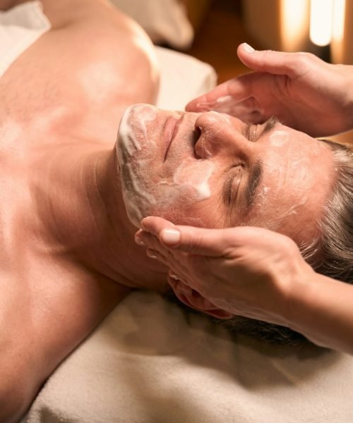 Qualified beautician cleansing man face before beauty procedure