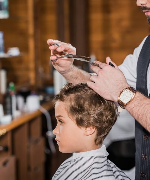 side view of barber cutting hair of curly little kid