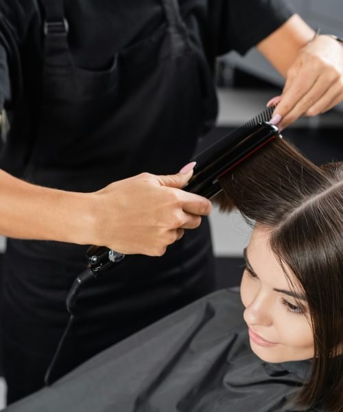 top view of professional hairdresser with hair straightener styling hair